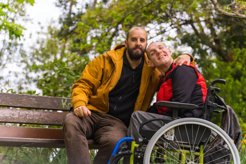 A person with a disability young man in a wheelchair with a friend on a bench in a public park in the city