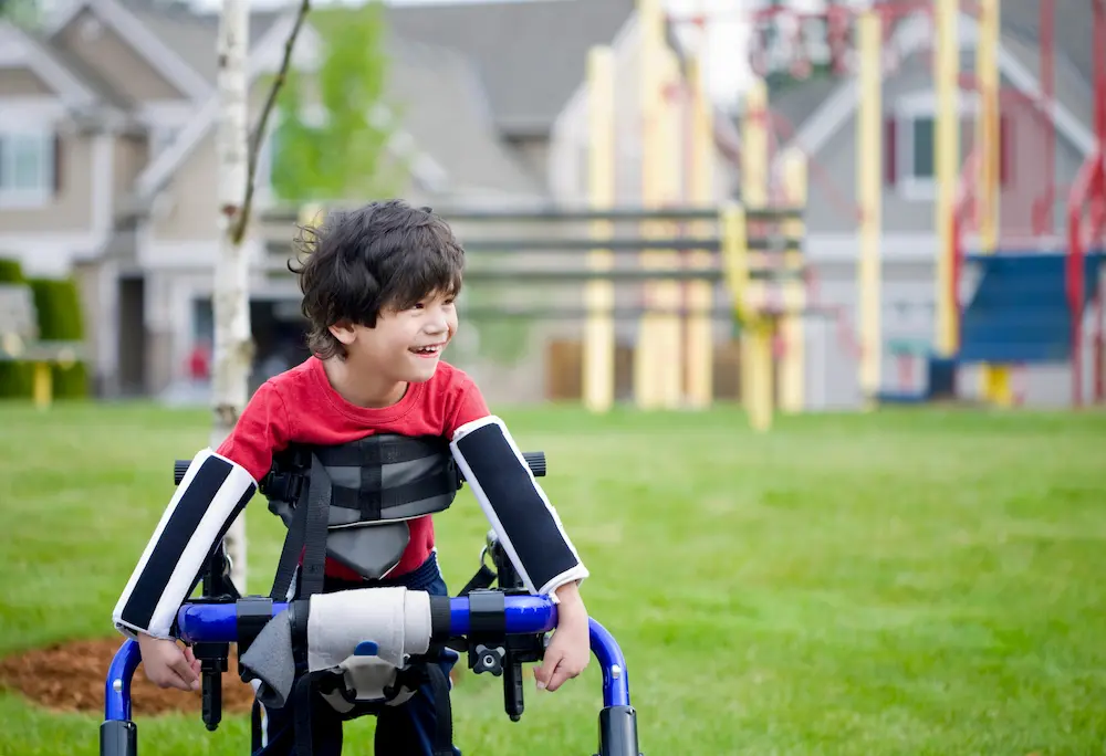Disabled four year old boy standing in walker near a playground