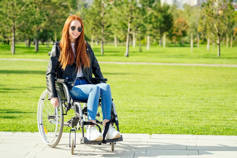 redhaired ginger woman feeing happy,she sitting wheelchair,wearing sunglasses and warm leather jacket in summer park
