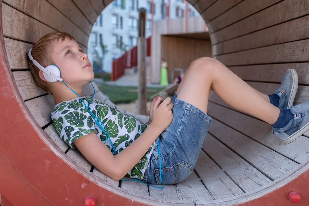 smiling boy with smartphone and headphones listening to music or playing game